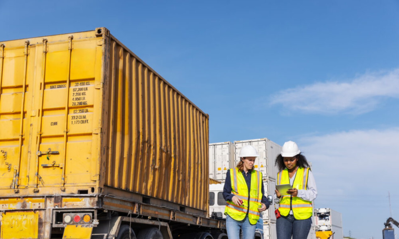 Two female workers in safety vests and hard hats at a worksite