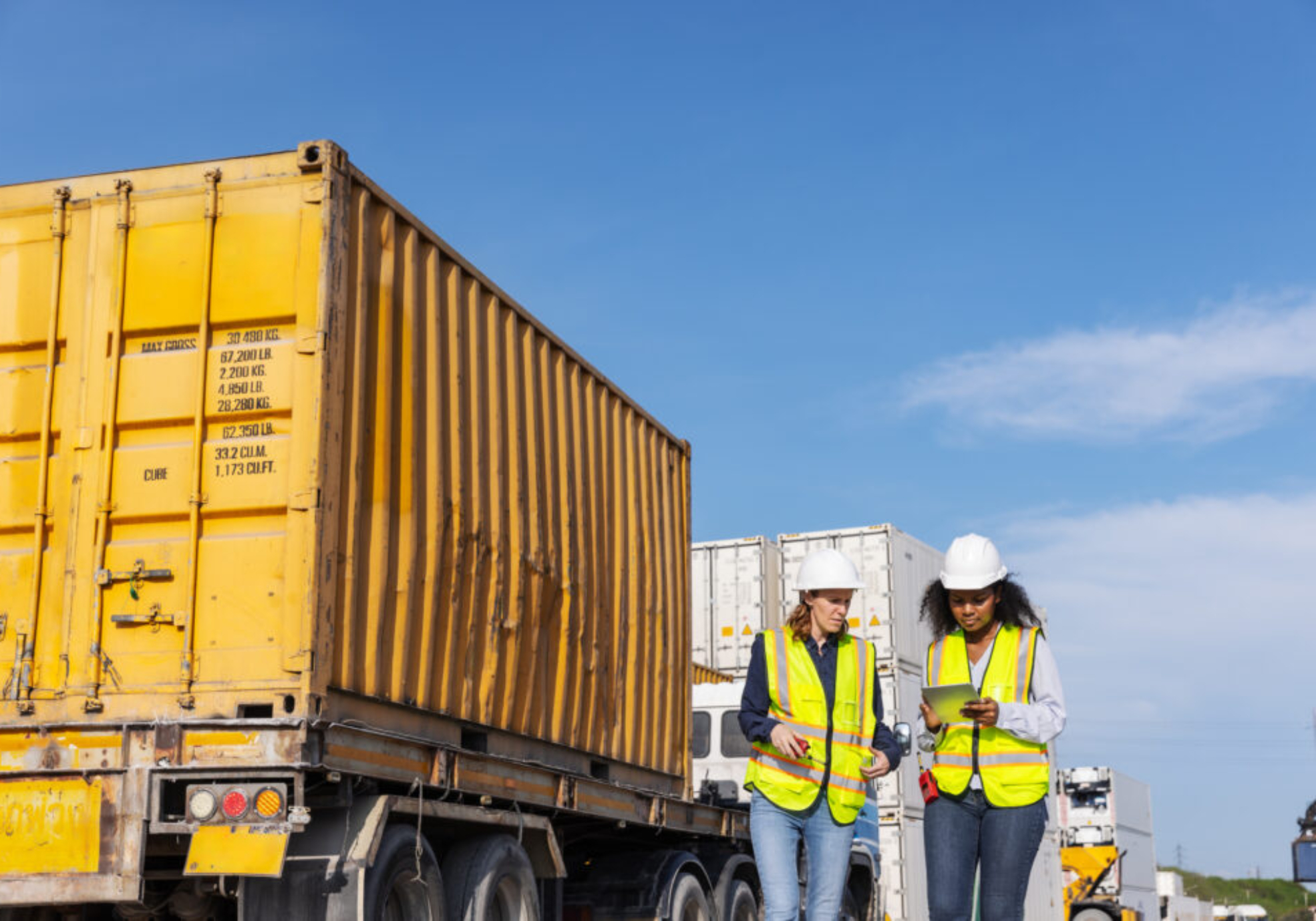 Two female workers in safety vests and hard hats at a worksite